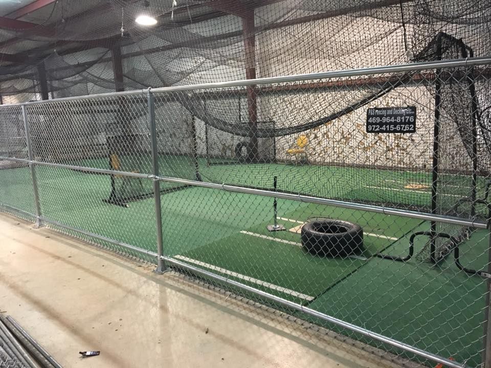 A chain link fence surrounds an indoor baseball field.