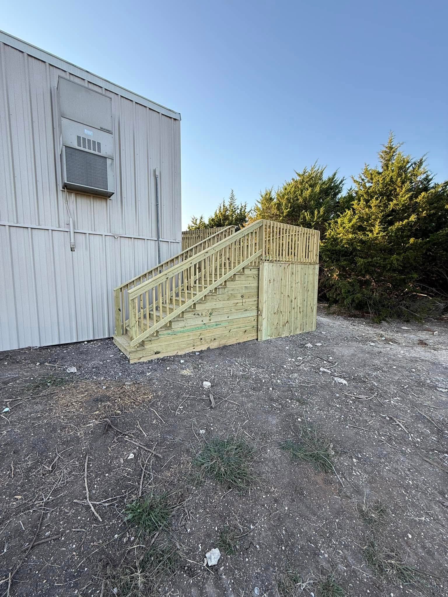 A white building with a wooden deck and stairs in front of it.