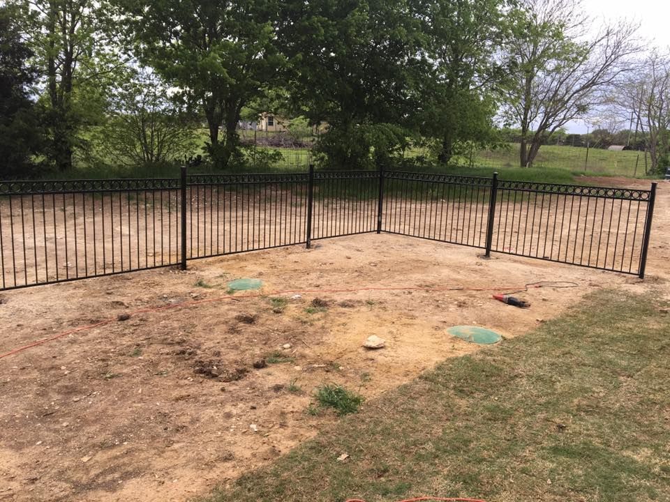 A black metal fence is surrounding a dirt field.