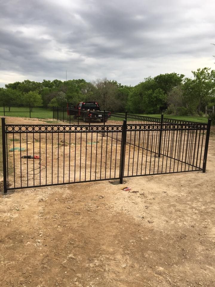 A metal fence surrounds a dirt field with trees in the background