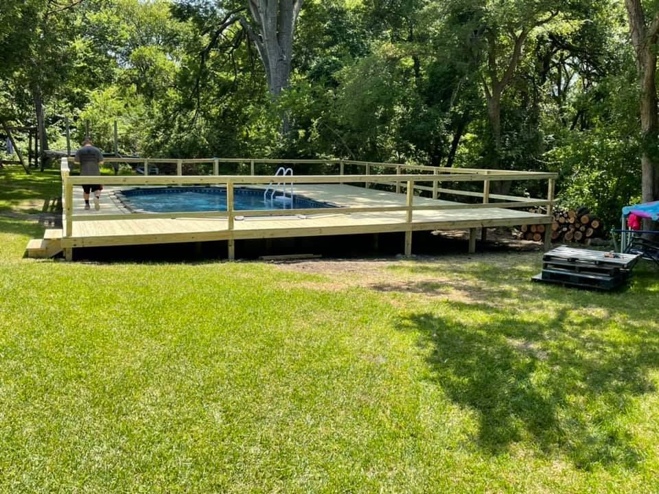 A wooden deck overlooking a swimming pool in a backyard.