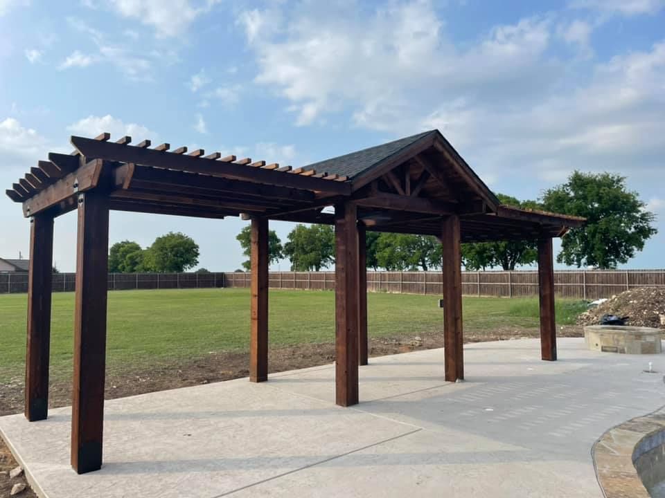 A wooden pergola is sitting in the middle of a grassy field