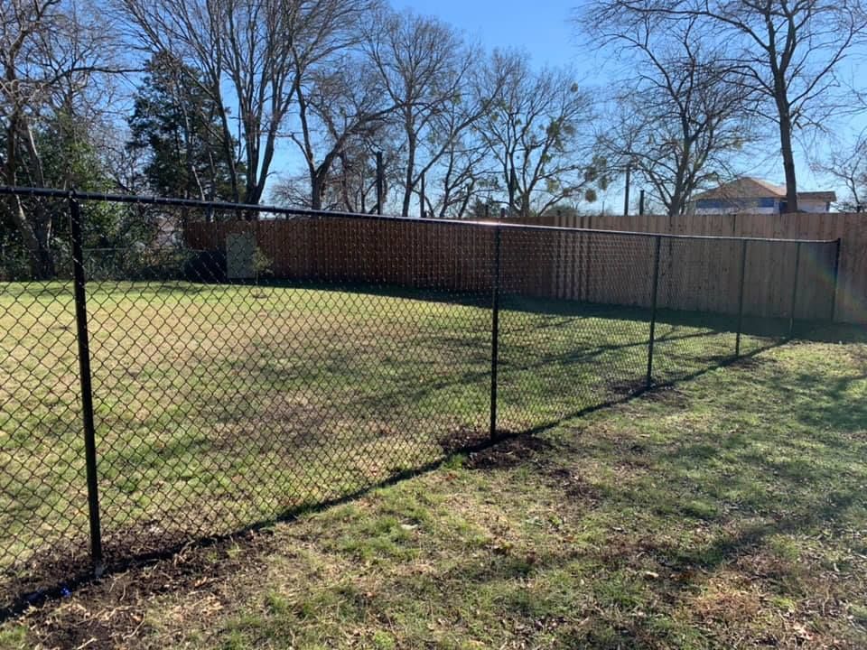 A chain link fence surrounds a grassy field with trees in the background.