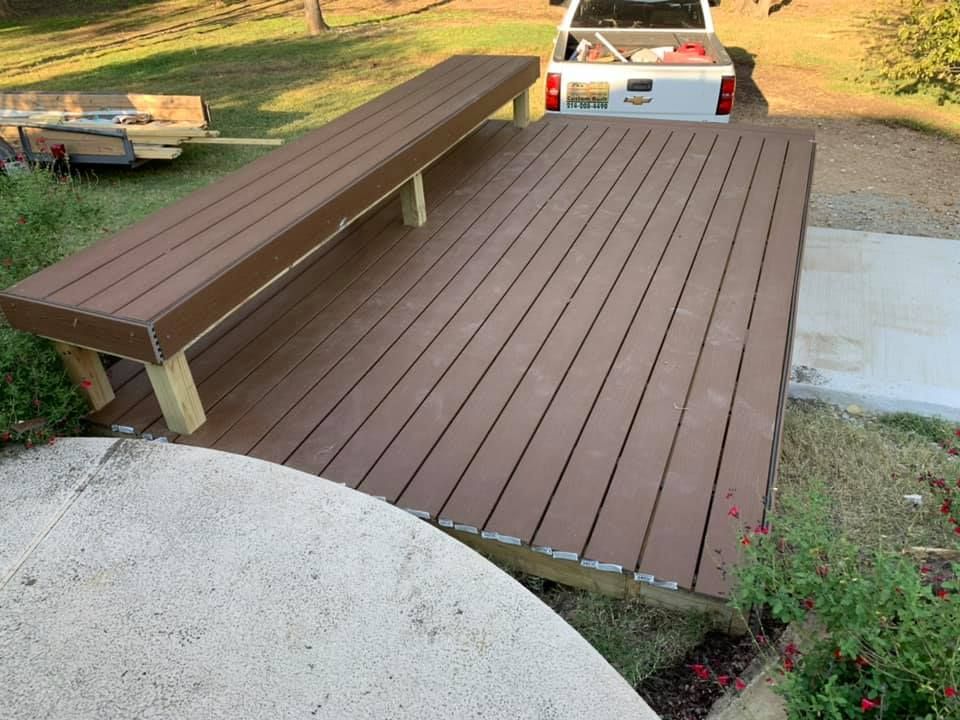 A wooden deck with a bench and a truck in the background.