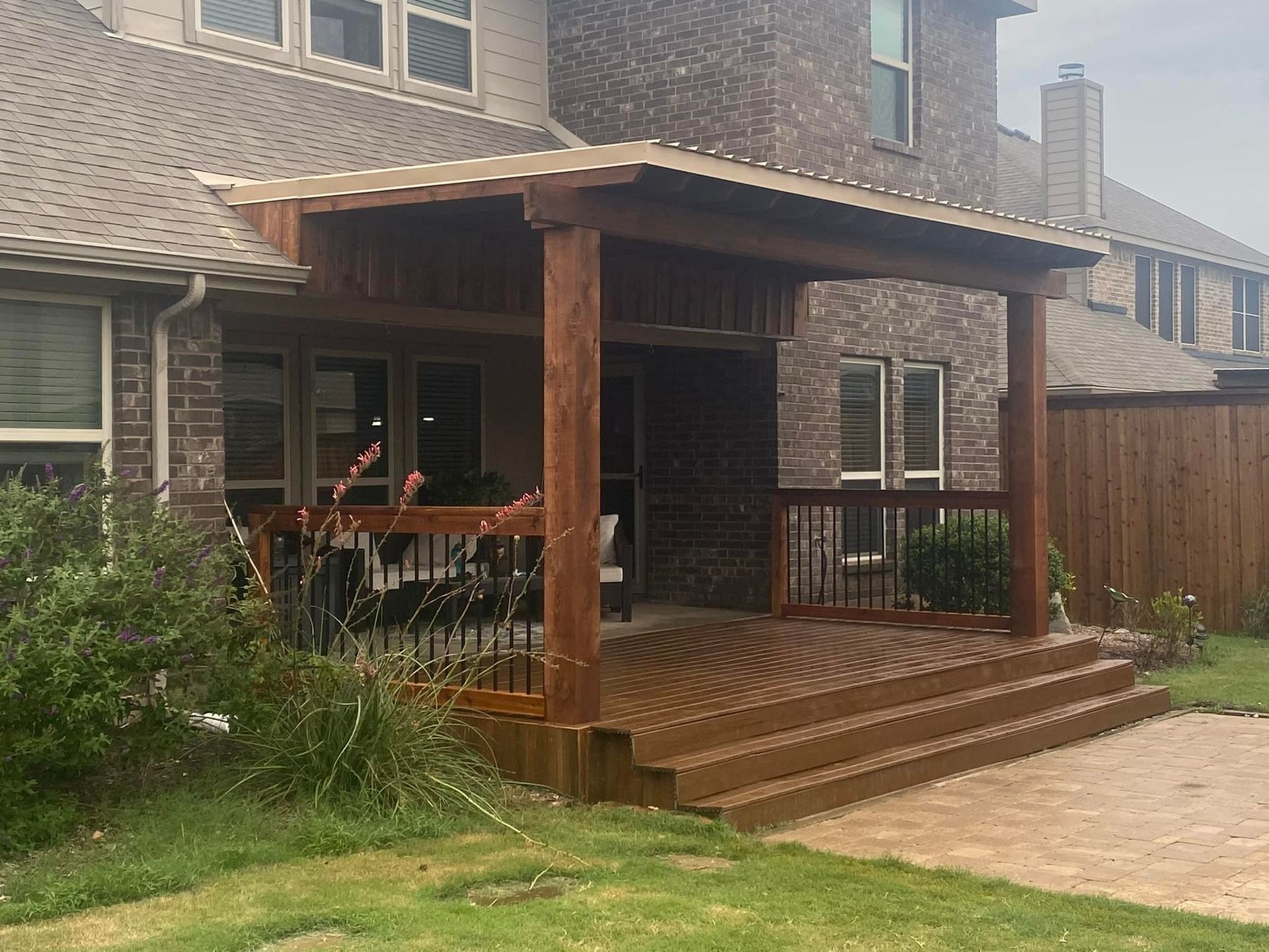 A wooden deck with a covered porch in front of a brick house.