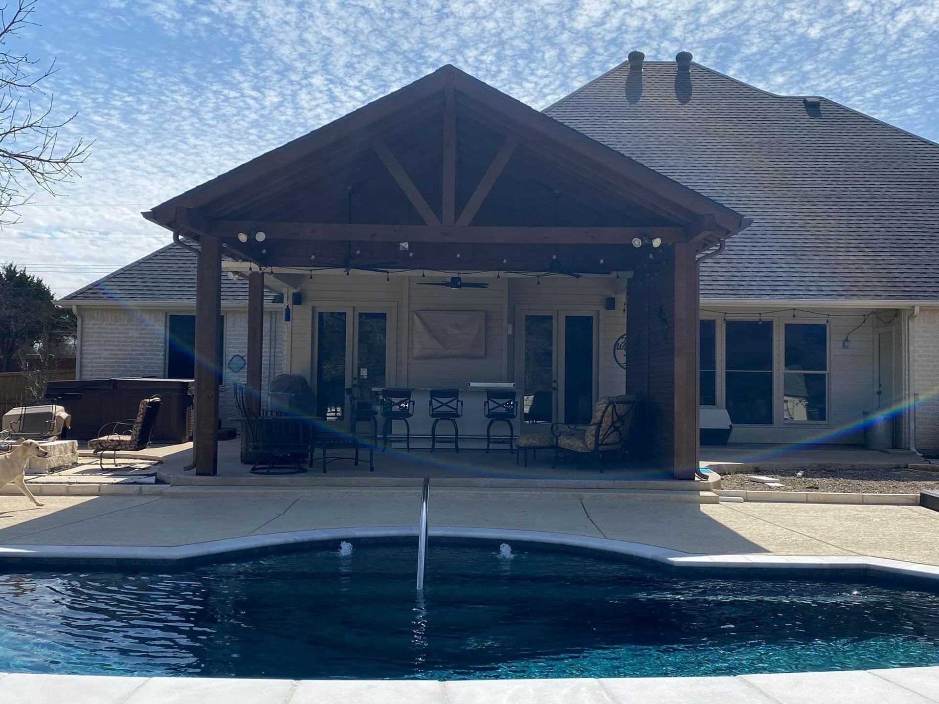A house with a covered patio and a pool in front of it.