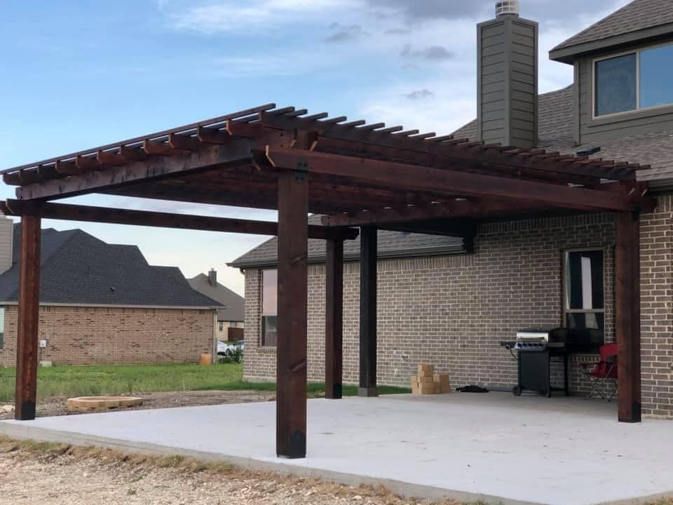 A wooden pergola is sitting in front of a brick house.