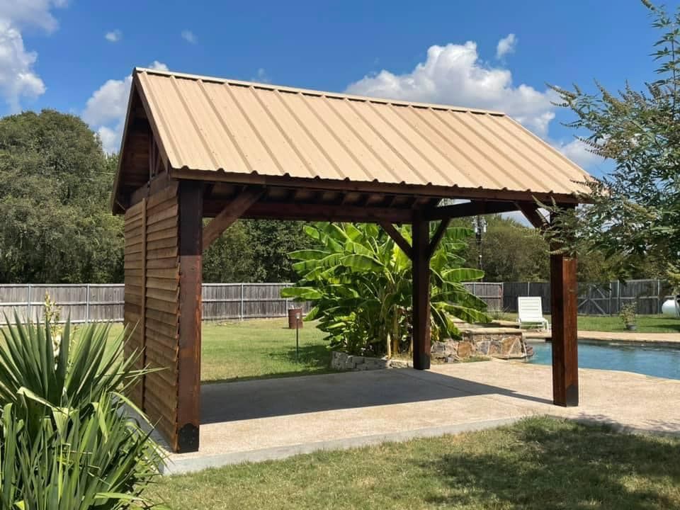 A wooden pavilion with a metal roof is next to a swimming pool.