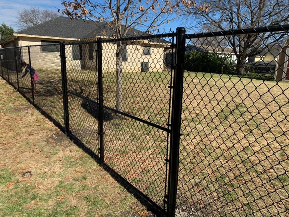 A black chain link fence surrounds a yard in front of a house.