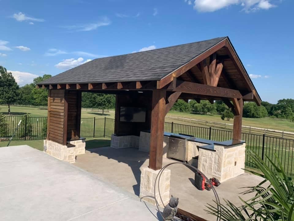 A wooden pavilion with a slate roof is sitting on top of a concrete patio.