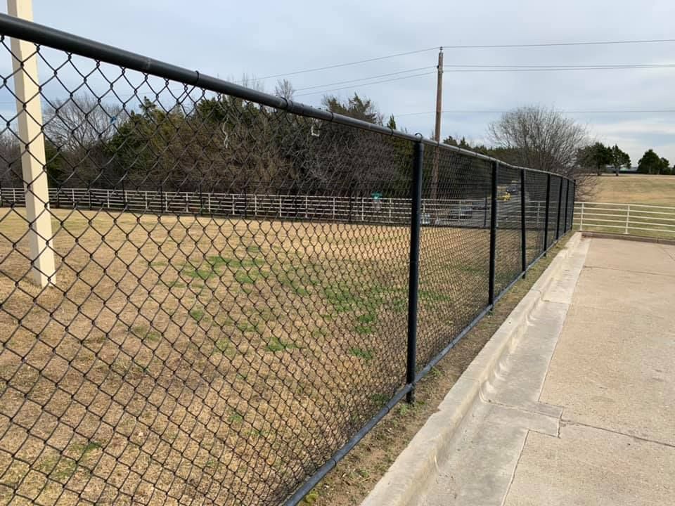 A chain link fence surrounds a field with trees in the background.