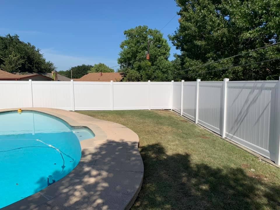 A white fence surrounds a swimming pool in a backyard.