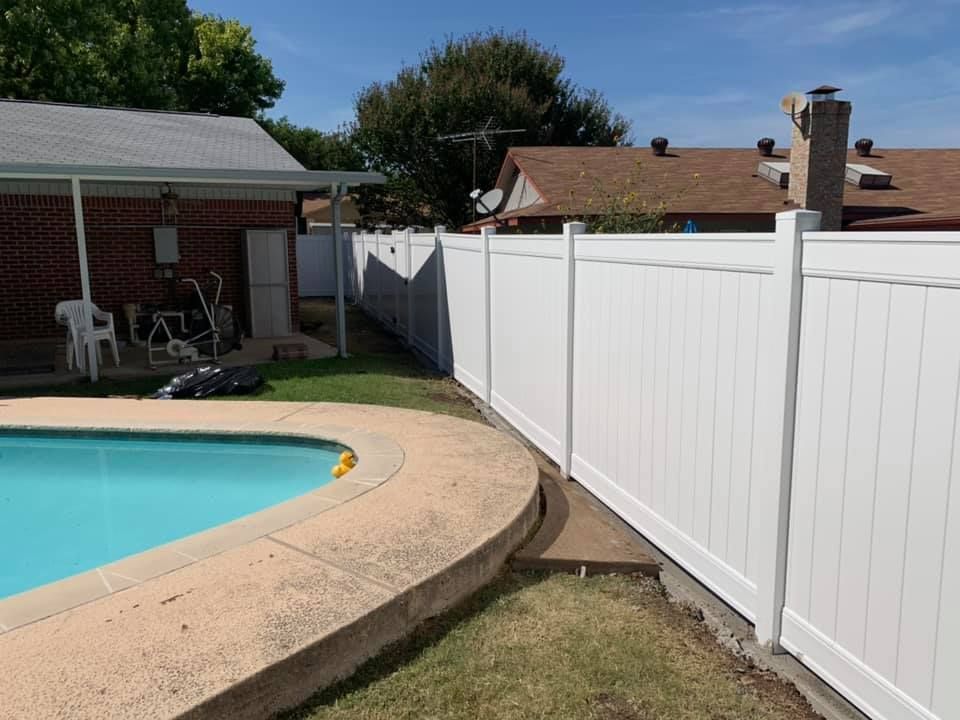A white fence surrounds a swimming pool in a backyard.