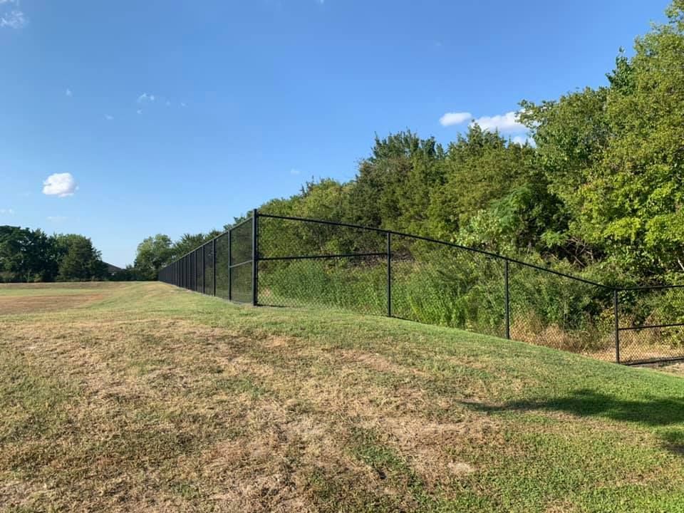 A chain link fence surrounds a grassy field with trees in the background.