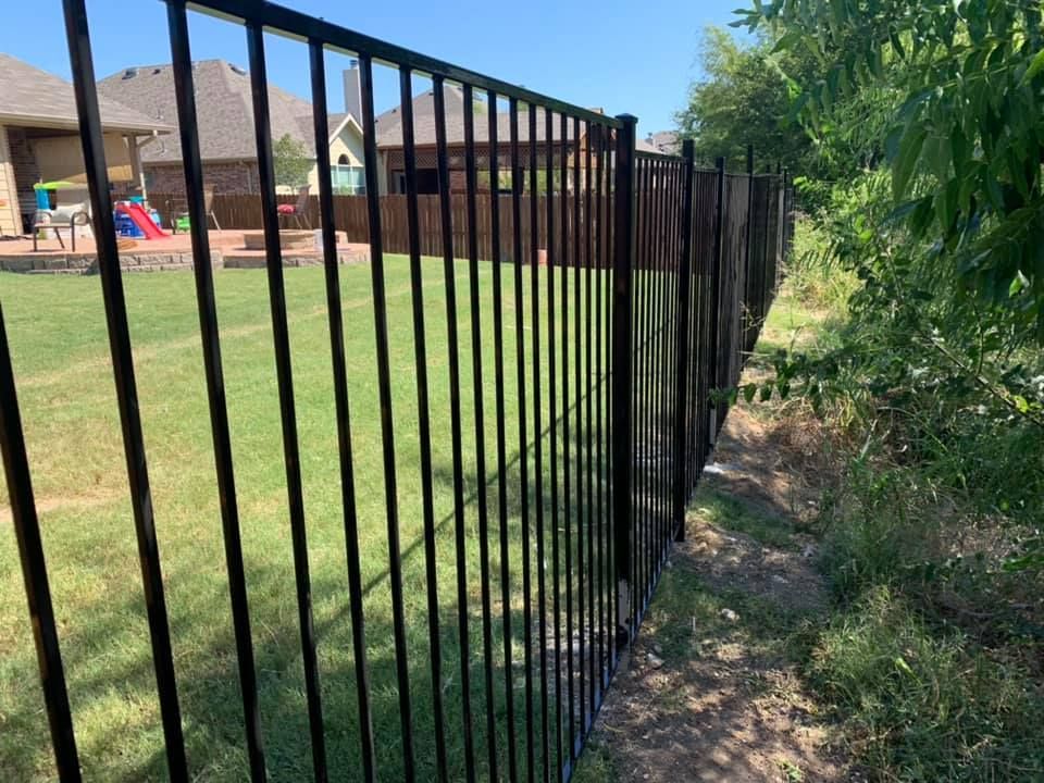 A black metal fence surrounds a lush green yard.