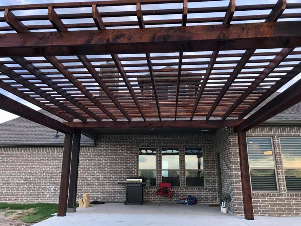 A wooden pergola is sitting in front of a brick house.