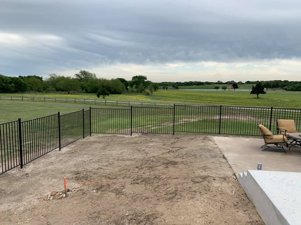 A fence surrounds a patio area with chairs and a table.