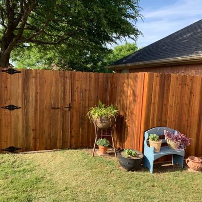A wooden fence with potted plants and a blue chair in front of it.