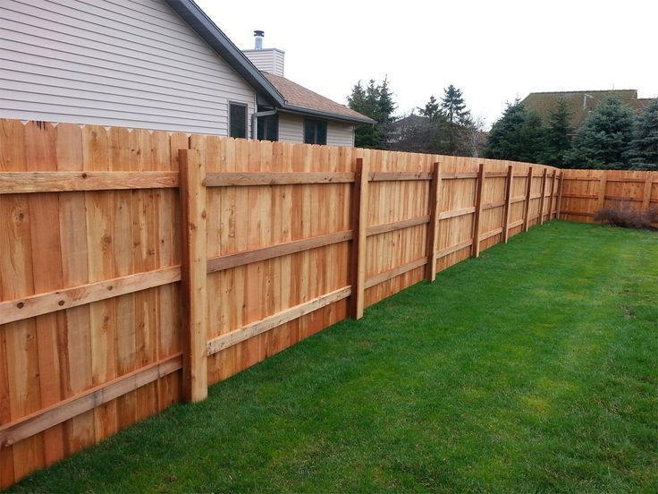 A wooden fence surrounds a lush green yard in front of a house