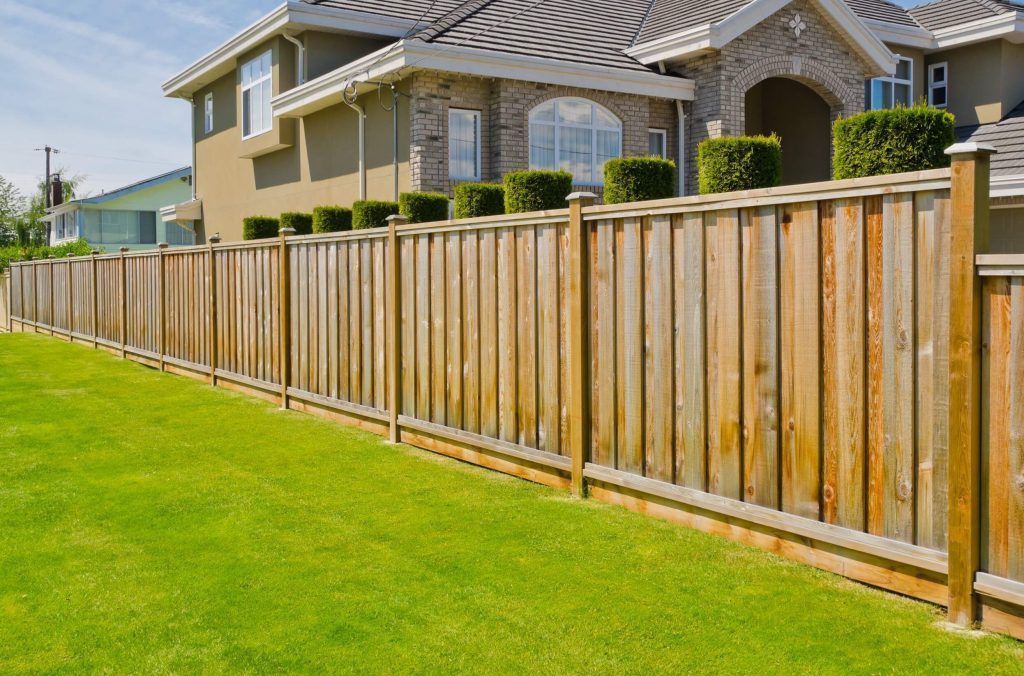 A wooden fence surrounds a lush green lawn in front of a house.