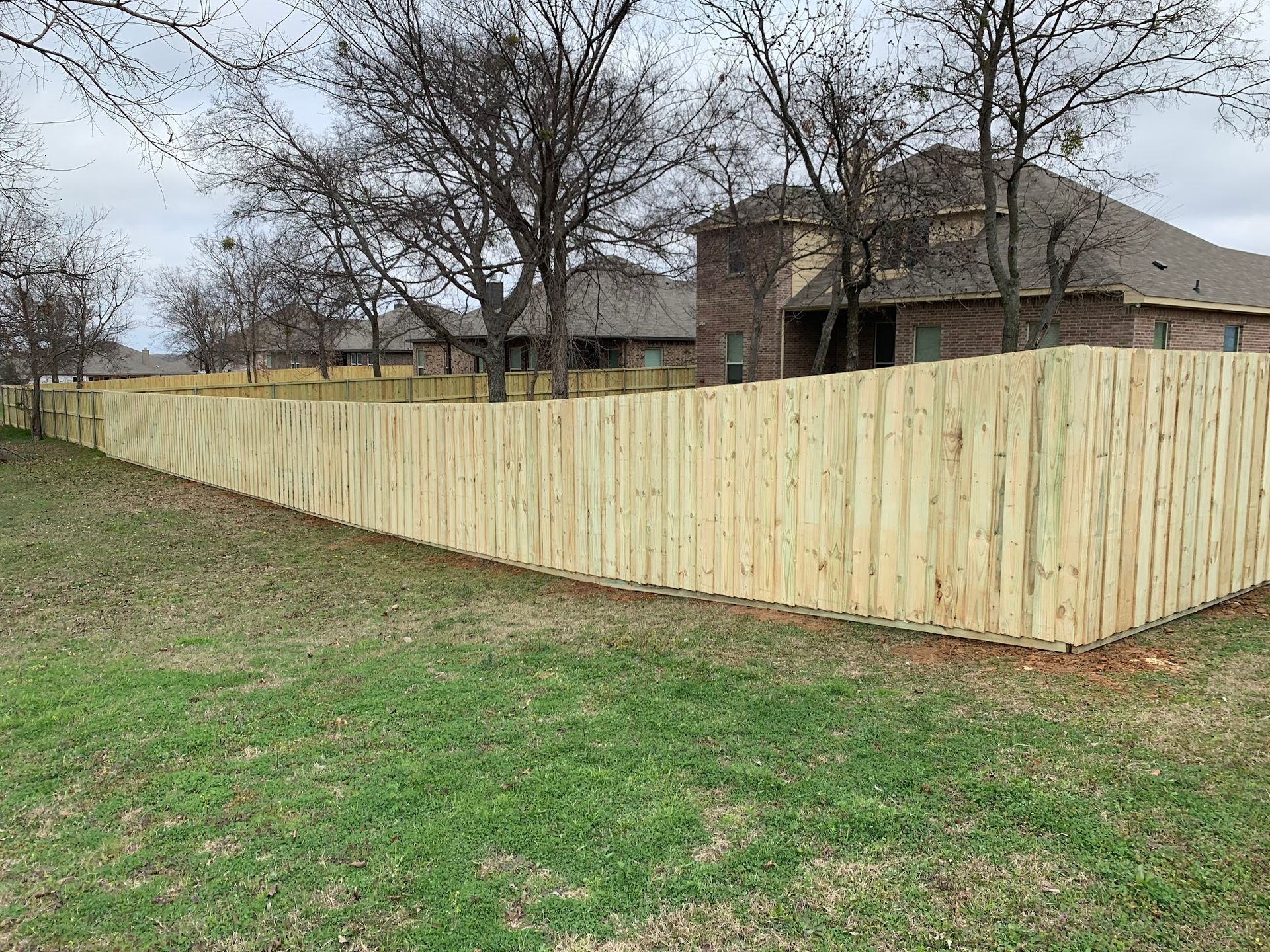 A wooden fence surrounds a lush green yard in front of a house.