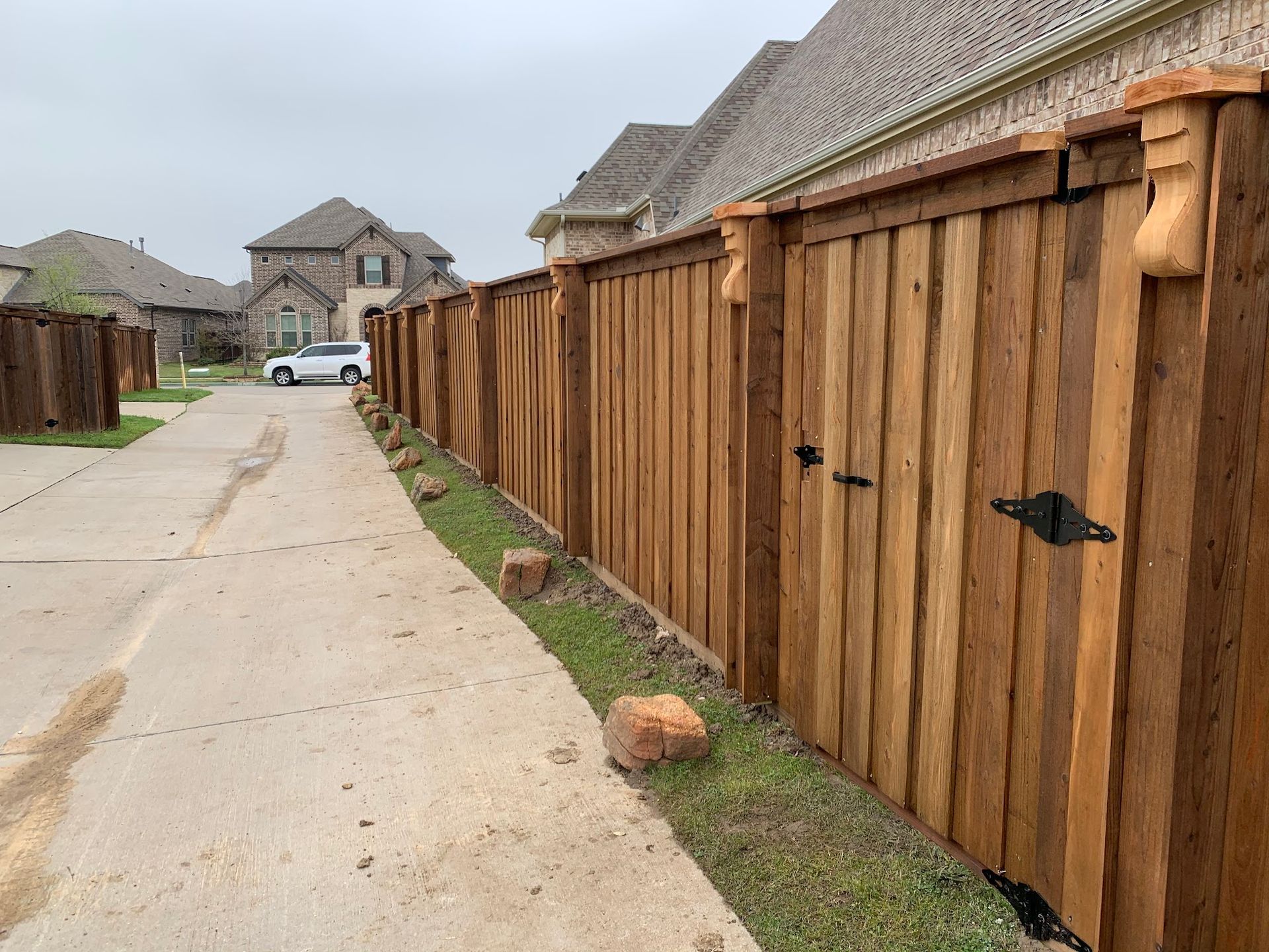 A wooden fence is along the side of a road next to a house.
