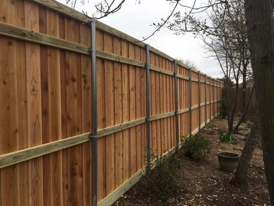 A wooden fence is surrounded by trees in a yard.