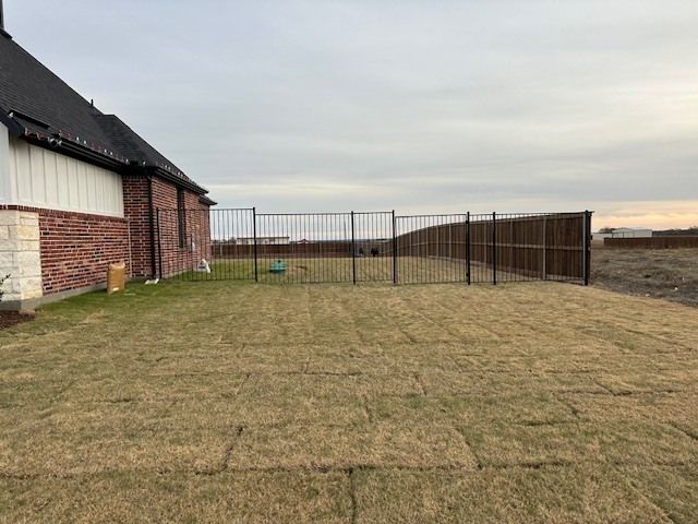 A backyard with a fence and a brick house in the background.