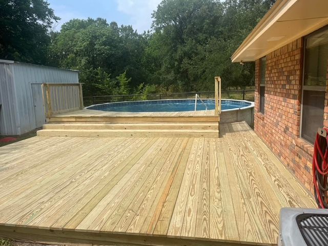 A wooden deck with a swimming pool in the background.