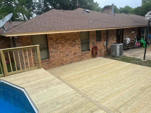 A wooden deck is sitting in front of a brick house next to a pool.