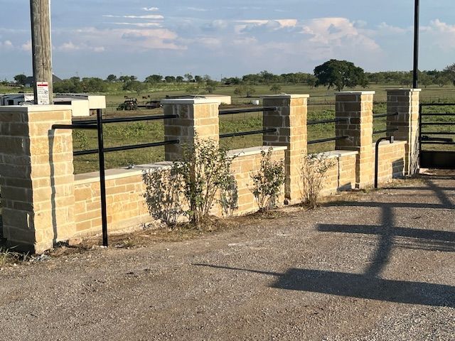 A brick wall with a metal fence in front of a field.