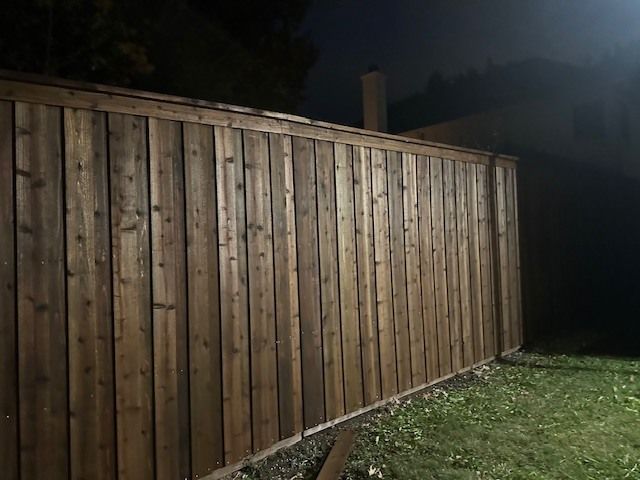 A wooden fence is lit up at night in a backyard.