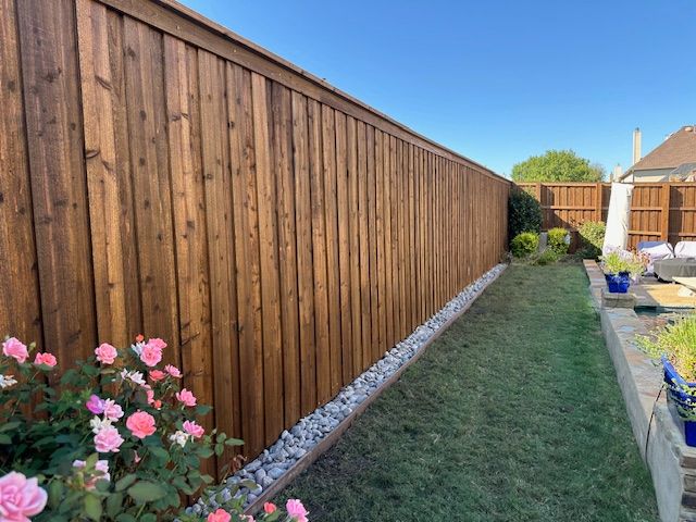 A wooden fence in a backyard with flowers in front of it.