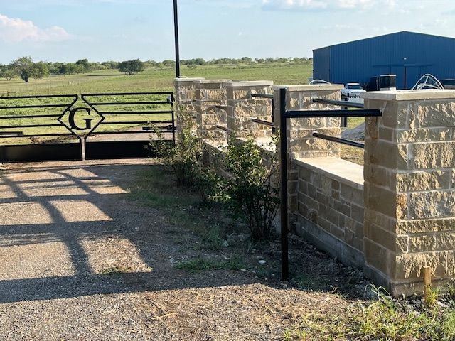 A gate with the letter g on it is next to a brick wall.