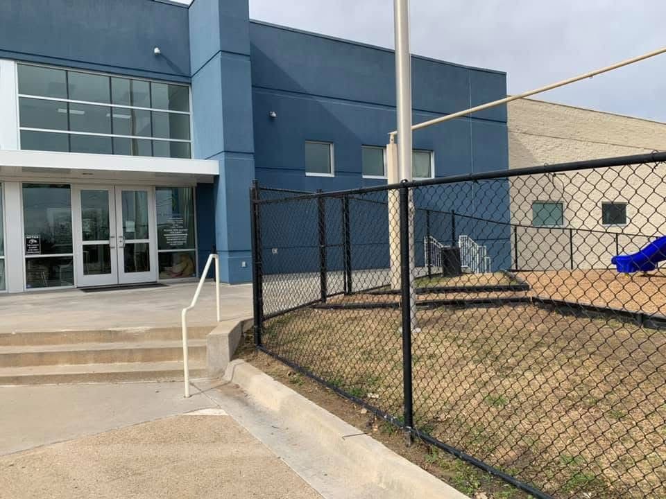 A chain link fence surrounds a playground in front of a building.