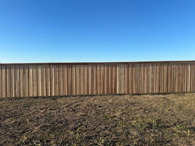 A wooden fence surrounds a dirt field with a blue sky in the background.