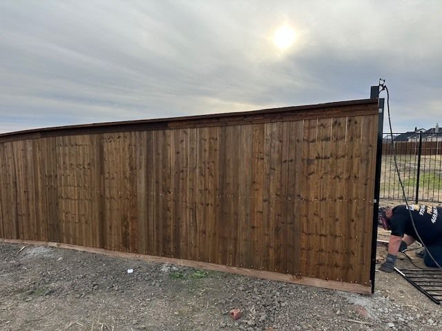 A man is working on a wooden fence in a dirt field.