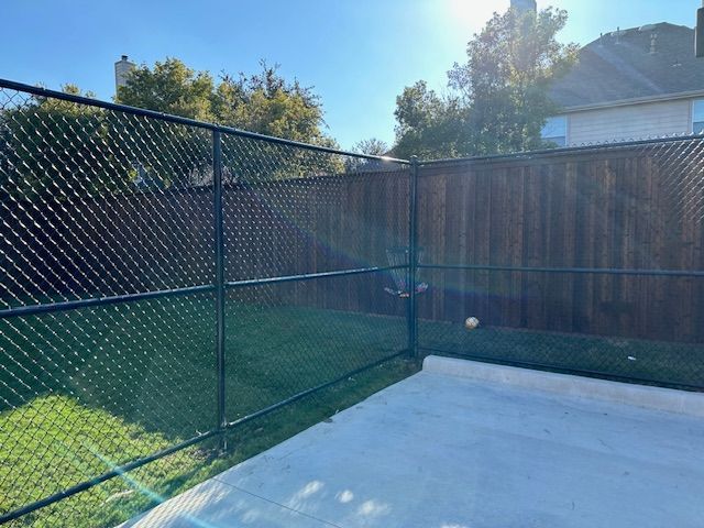 A chain link fence surrounds a basketball court in a backyard.