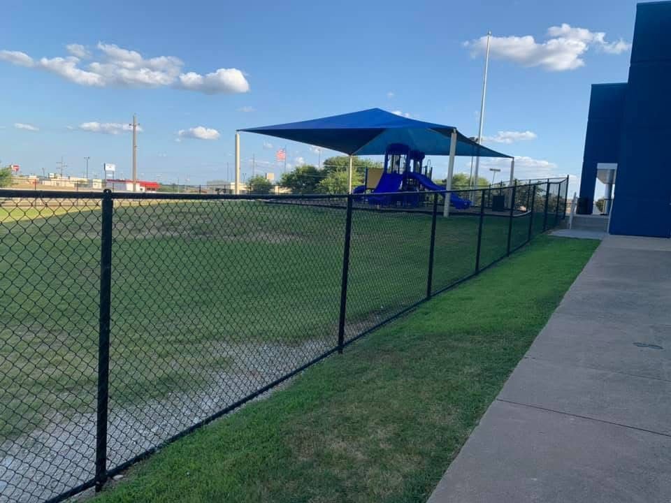 A chain link fence surrounds a playground in a park.