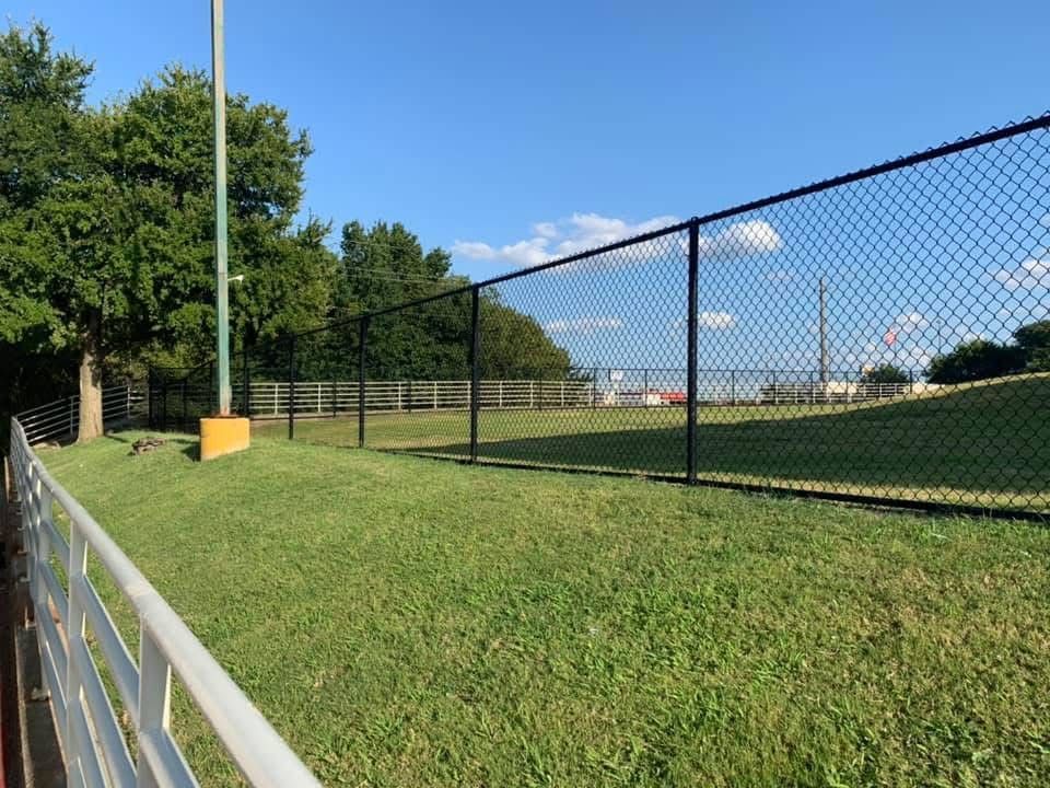 A chain link fence surrounds a lush green field.