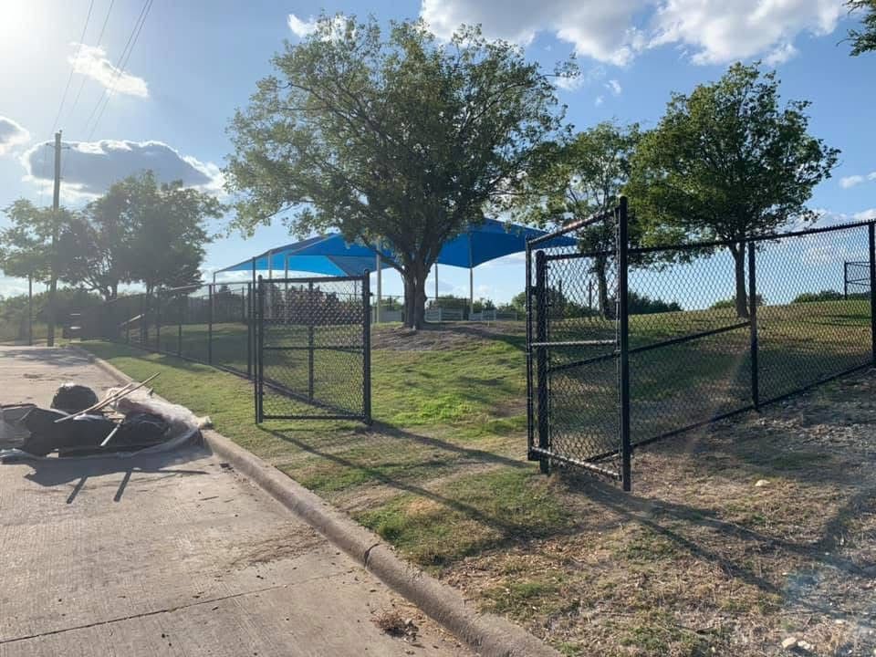 A chain link fence with a blue umbrella on top of it in a park.