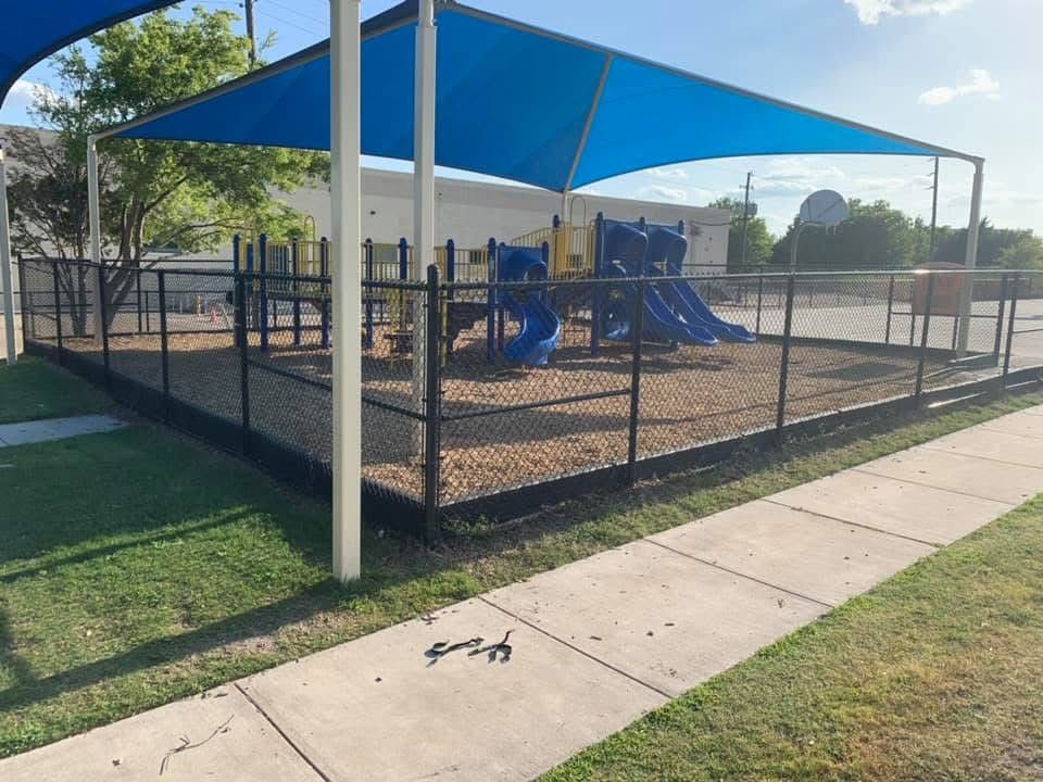 A playground with a blue umbrella and a fence around it