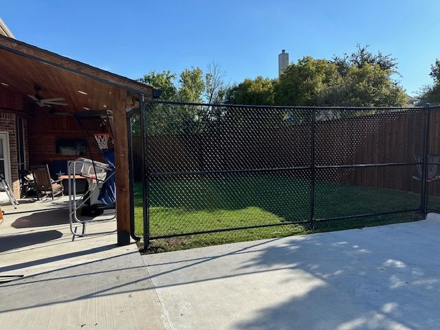 A chain link fence surrounds a basketball court in a backyard.