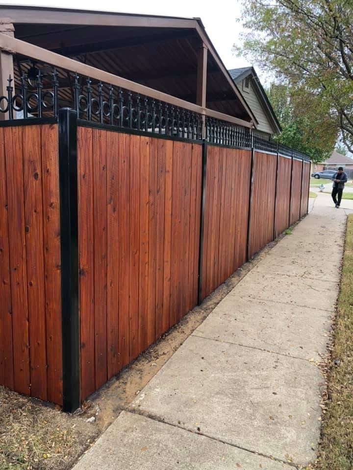 A man is walking down a sidewalk next to a wooden fence.