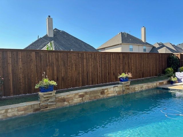 A wooden fence surrounds a large swimming pool.