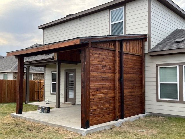 A house with a covered patio and a wooden wall in the backyard.