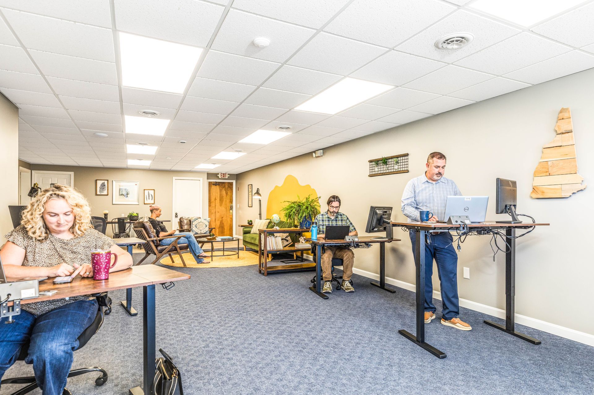 A bright office workspace with three people working at desks, including one person using a standing desk.