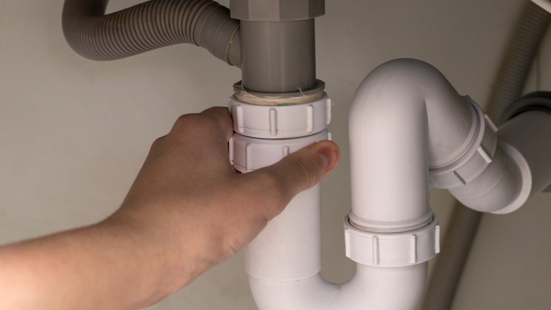 A person is fixing a sink pipe with their hand.