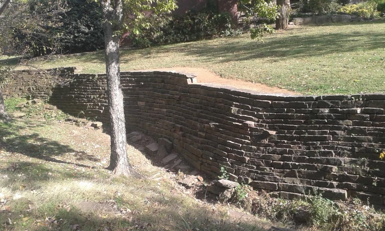 Brick retaining wall next to a grassy hill, with a small tree in front.