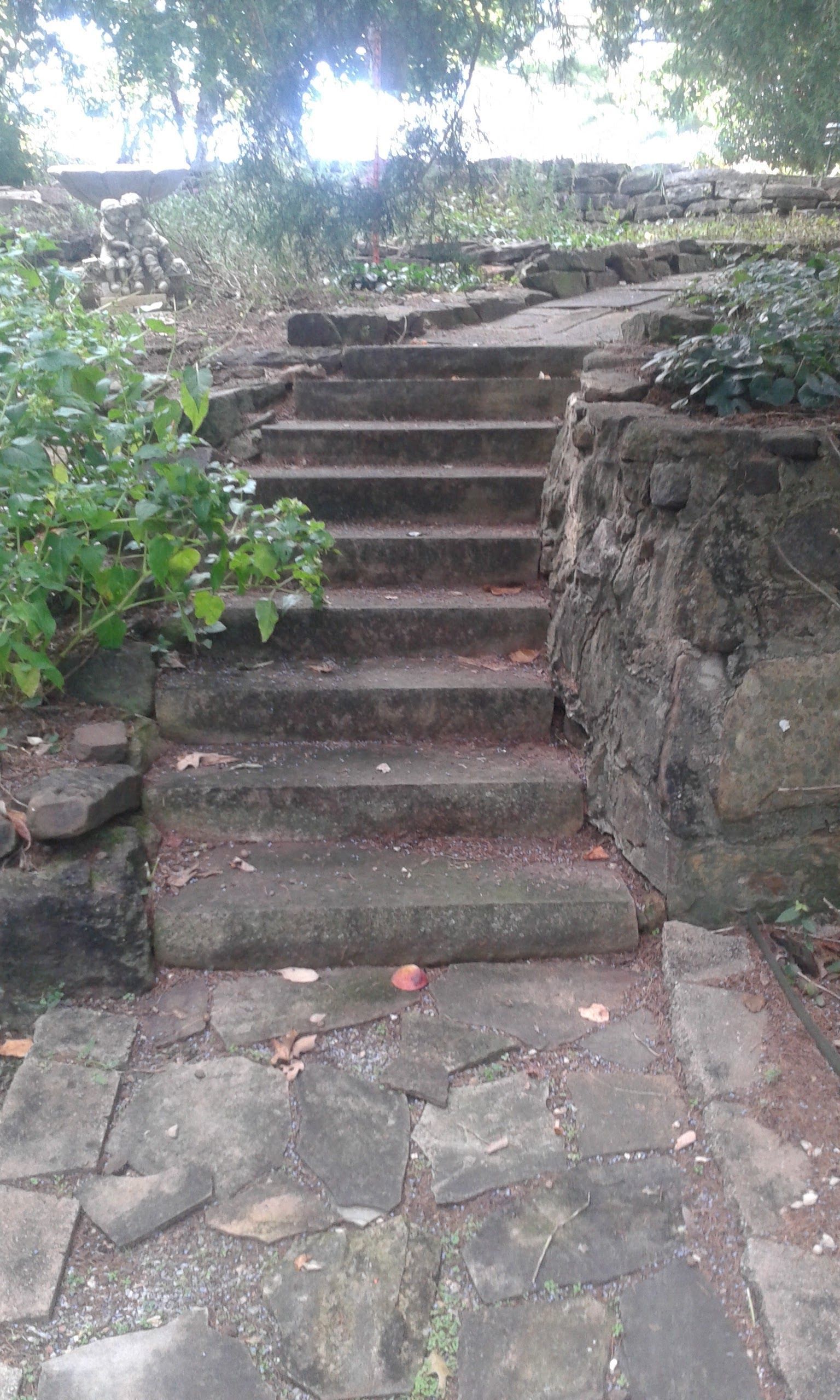 Stone steps lead upwards, flanked by stone walls and greenery, in an outdoor setting.
